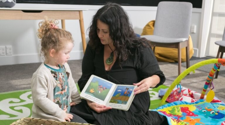 Woman sitting on floor reading a picture book to a young girl
