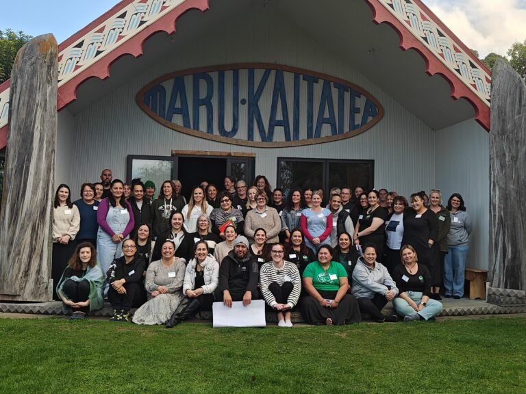 Group of 40 or so people sitting on the porch of Takahanga Marae